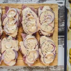 Schab pieczony w plastrach, polany kremowym sosem i posypany ziołami, obok pieczone ziemniaki.