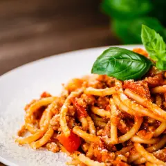 Talerz spaghetti bolognese z bazylią i parmezanem na drewnianym tle.