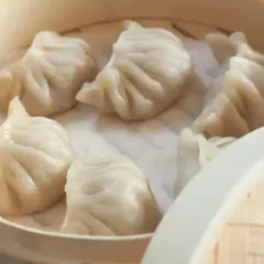 Parujące pierożki dim sum w bambusowym parowniku, gotowe do podania.