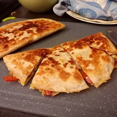 Złocista quesadilla, pokrojona na trójkąty, z widocznym nadzieniem z papryki. Idealny przepis na szybki posiłek.
