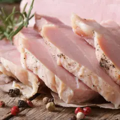 Super delikatny i soczysty schab gotowany, pokrojony w plastry, z gałązką rozmarynu i ziarnami pieprzu na drewnianym tle.