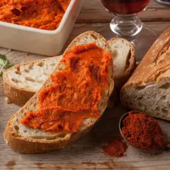 Nduja co to? Pikantna, pomarańczowa pasta na chlebie, obok świeżego pieczywa, papryki i ziół.