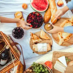 Piknikowy koc z owocami, pieczywem, serami, przekąskami i koszykiem.
