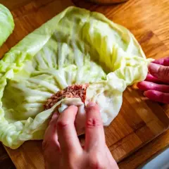 Ręce zwijają gołąbki z farszem mięsnym w liście kapusty. To początek przygotowań do pysznego dania, idealnego na przepis na gołąbki na 1kg mięsa.