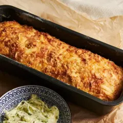 Złocista babka ziemniaczana prosto z piekarnika, pachnąca jak u babci. Obok miseczka z ziołowym masełkiem.
