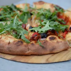 Pizza z rukolą i oliwkami na drewnianej desce.