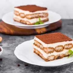Pyszne tiramisu z warstwami kremu i biszkoptów do tiramisu, posypane kakao. Obok filiżanka kawy i ziarna kawy.