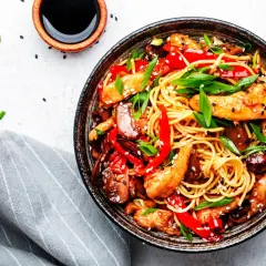 Pyszny kurczak po tajlandzku z makaronem, papryką i szczypiorkiem, posypany sezamem.