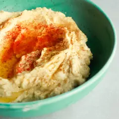 Kremowy hummus w turkusowej misce, posypany papryką i skropiony oliwą. Idealny do domowego hummusu przepis.