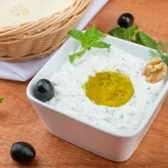Jak zrobić tzatziki? Kremowy dip jogurtowy z oliwą, miętą, orzechami i oliwkami. Obok koszyk z pitą.