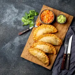 Złociste empanadas na desce, podane z salsą pomidorową i guacamole. Idealne na przekąskę.