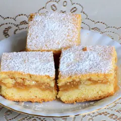 Trzy kawałki ekspresowego ciasta z jabłkami, posypane cukrem pudrem, na białym talerzyku.