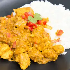 Aromatyczny kurczak curry z ryżem, udekorowany papryką i kolendrą, podany na czarnym talerzu.