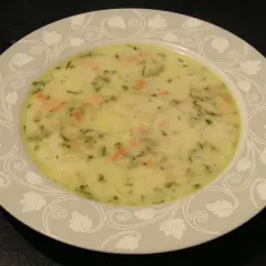 Talerz z kremową zupą ogórkową z widocznymi kawałkami warzyw i ziół.