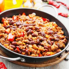 Pyszne chili con carne przepis w głębokiej patelni, z fasolą, mięsem mielonym i papryką. Obok pomidory i papryczki chili.