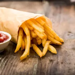 Frytki w papierowej torbie z ketchupem na drewnianym stole.