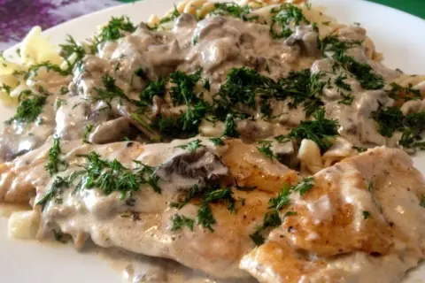 Pyszny kurczak z mascarpone i grzybami w kremowym sosie, podany z makaronem i posypany świeżym koperkiem.
