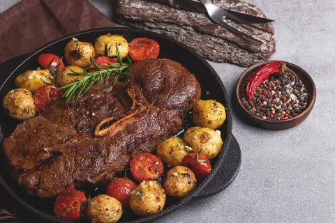 Stek z dziczyzny z pieczonymi ziemniakami, pomidorkami i mieszanką pieprzu.