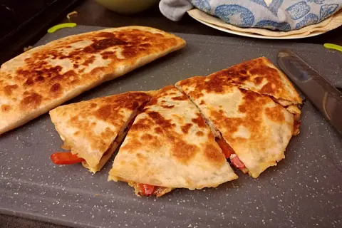 Złocista quesadilla, pokrojona na trójkąty, z widocznym nadzieniem z papryki. Idealny przepis na szybki posiłek.