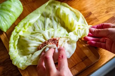 Ręce zwijają gołąbki z farszem mięsnym w liście kapusty. To początek przygotowań do pysznego dania, idealnego na przepis na gołąbki na 1kg mięsa.