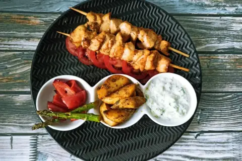 Dwa szaszłyki z kurczaka, czyli pyszne souvlaki, podane z pieczonymi ziemniakami, papryką, szparagami i sosem tzatziki.