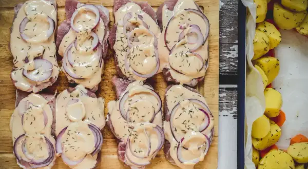 Schab pieczony w plastrach, polany kremowym sosem i posypany ziołami, obok pieczone ziemniaki.
