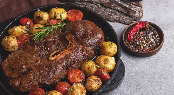 Stek z dziczyzny z pieczonymi ziemniakami, pomidorkami i mieszanką pieprzu.