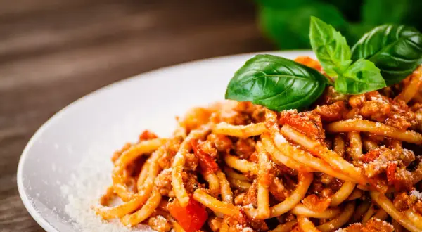 Talerz spaghetti bolognese z bazylią i parmezanem na drewnianym tle.