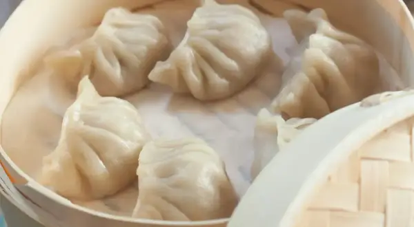 Parujące pierożki dim sum w bambusowym parowniku, gotowe do podania.