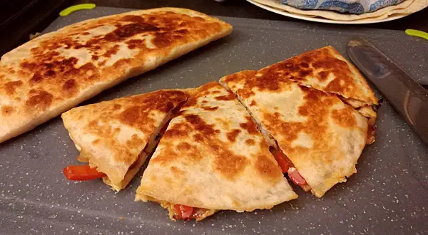 Złocista quesadilla, pokrojona na trójkąty, z widocznym nadzieniem z papryki. Idealny przepis na szybki posiłek.