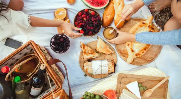 Piknikowy koc z owocami, pieczywem, serami, przekąskami i koszykiem.