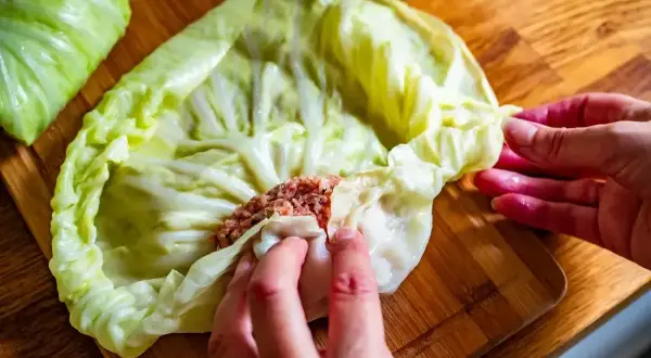 Ręce zwijają gołąbki z farszem mięsnym w liście kapusty. To początek przygotowań do pysznego dania, idealnego na przepis na gołąbki na 1kg mięsa.