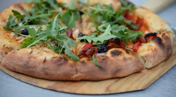 Pizza z rukolą i oliwkami na drewnianej desce.