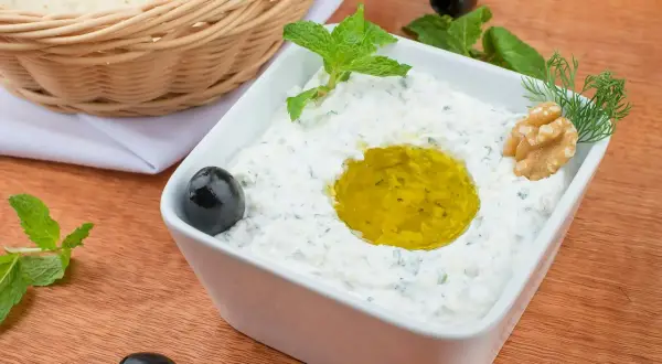 Jak zrobić tzatziki? Kremowy dip jogurtowy z oliwą, miętą, orzechami i oliwkami. Obok koszyk z pitą.