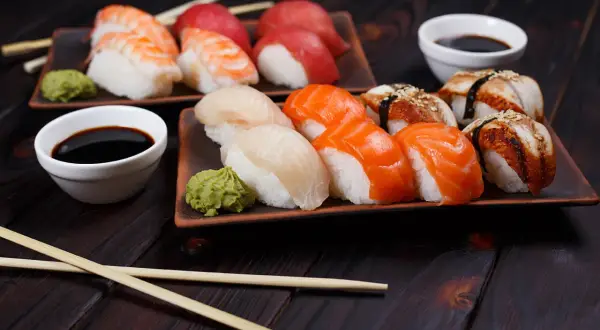 Różnorodne sushi rodzaje: nigiri z krewetką, łososiem, białym rybą i węgorzem, podane z wasabi i sosem sojowym.