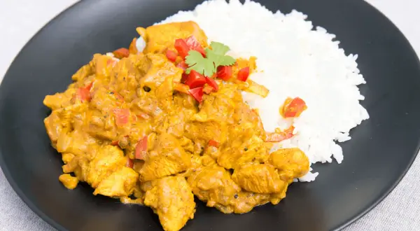Aromatyczny kurczak curry z ryżem, udekorowany papryką i kolendrą, podany na czarnym talerzu.