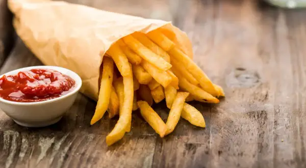Frytki w papierowej torbie z ketchupem na drewnianym stole.