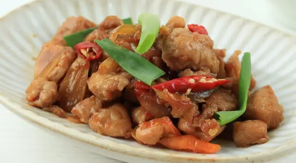 Pyszny kurczak po wietnamsku z papryczkami chili i zieloną cebulką na talerzu.