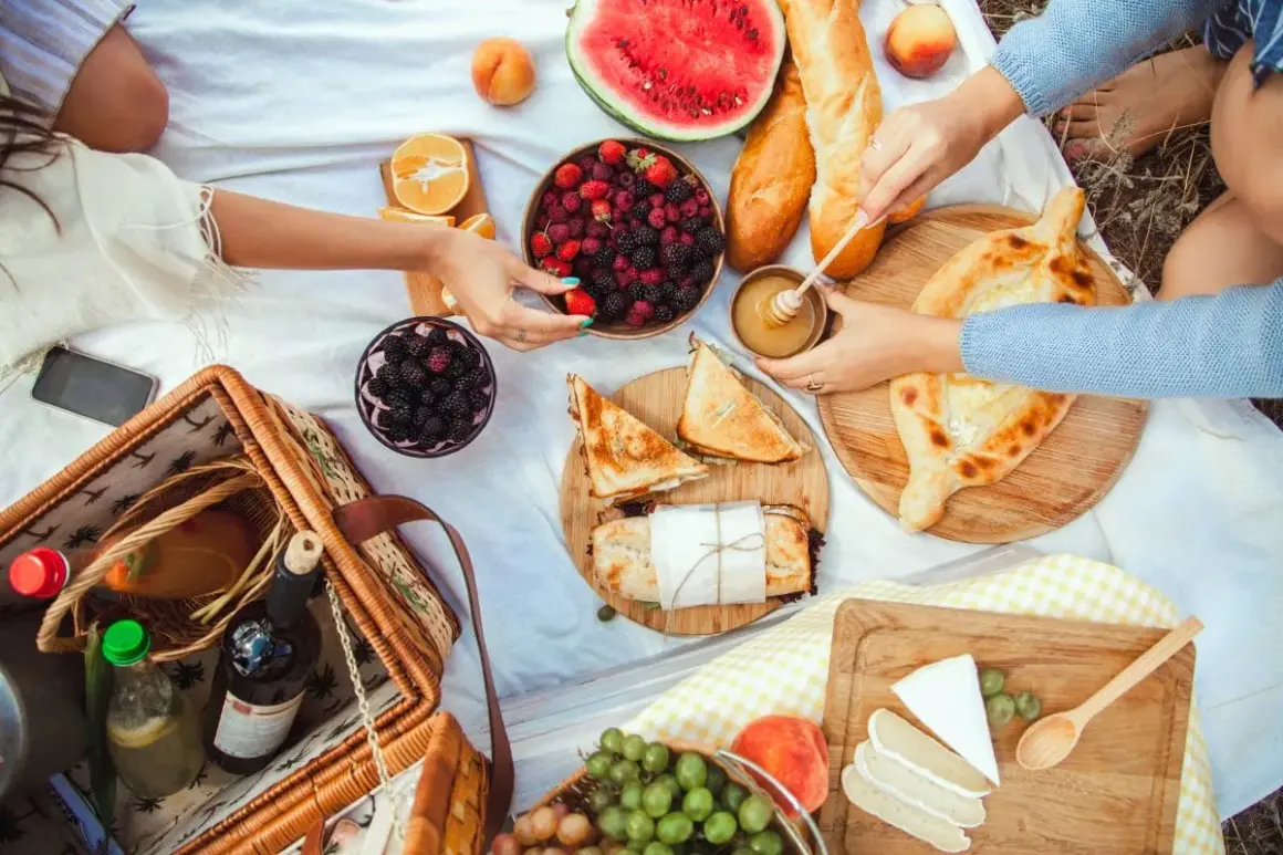 Piknikowy koc z owocami, pieczywem, serami, przekąskami i koszykiem.