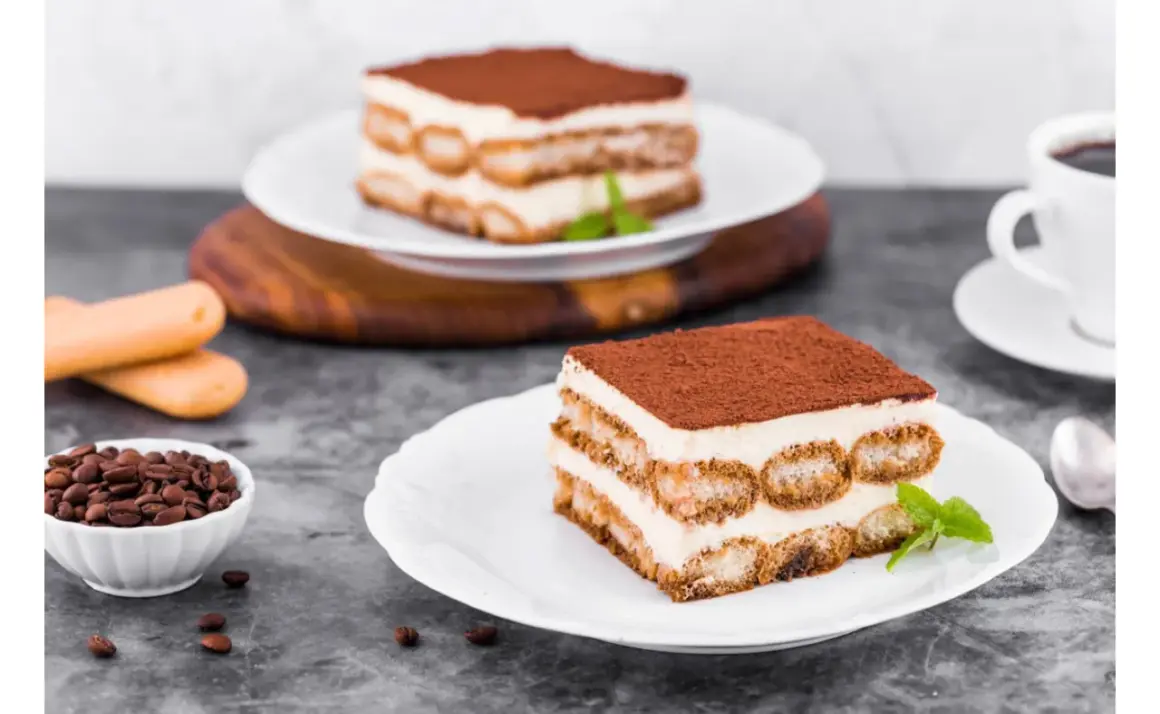 Pyszne tiramisu z warstwami kremu i biszkoptów do tiramisu, posypane kakao. Obok filiżanka kawy i ziarna kawy.