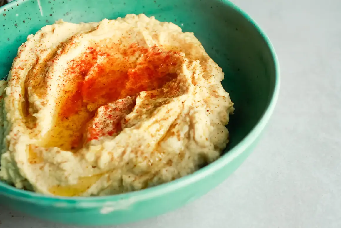 Kremowy hummus w turkusowej misce, posypany papryką i skropiony oliwą. Idealny do domowego hummusu przepis.