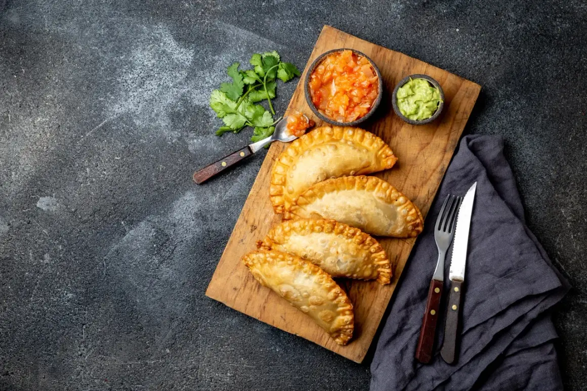Złociste empanadas na desce, podane z salsą pomidorową i guacamole. Idealne na przekąskę.