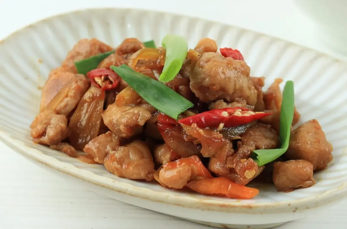 Pyszny kurczak po wietnamsku z papryczkami chili i zieloną cebulką na talerzu.
