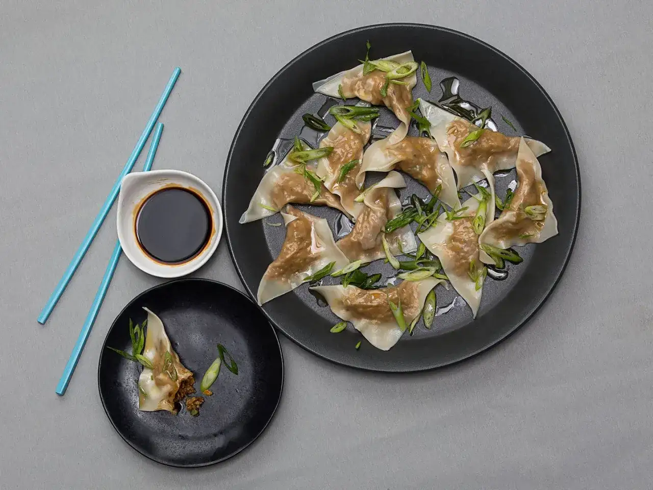 Pyszne pierożki gyoza, przypominające kształtem małe empanadas, podane z sosem sojowym i szczypiorkiem.