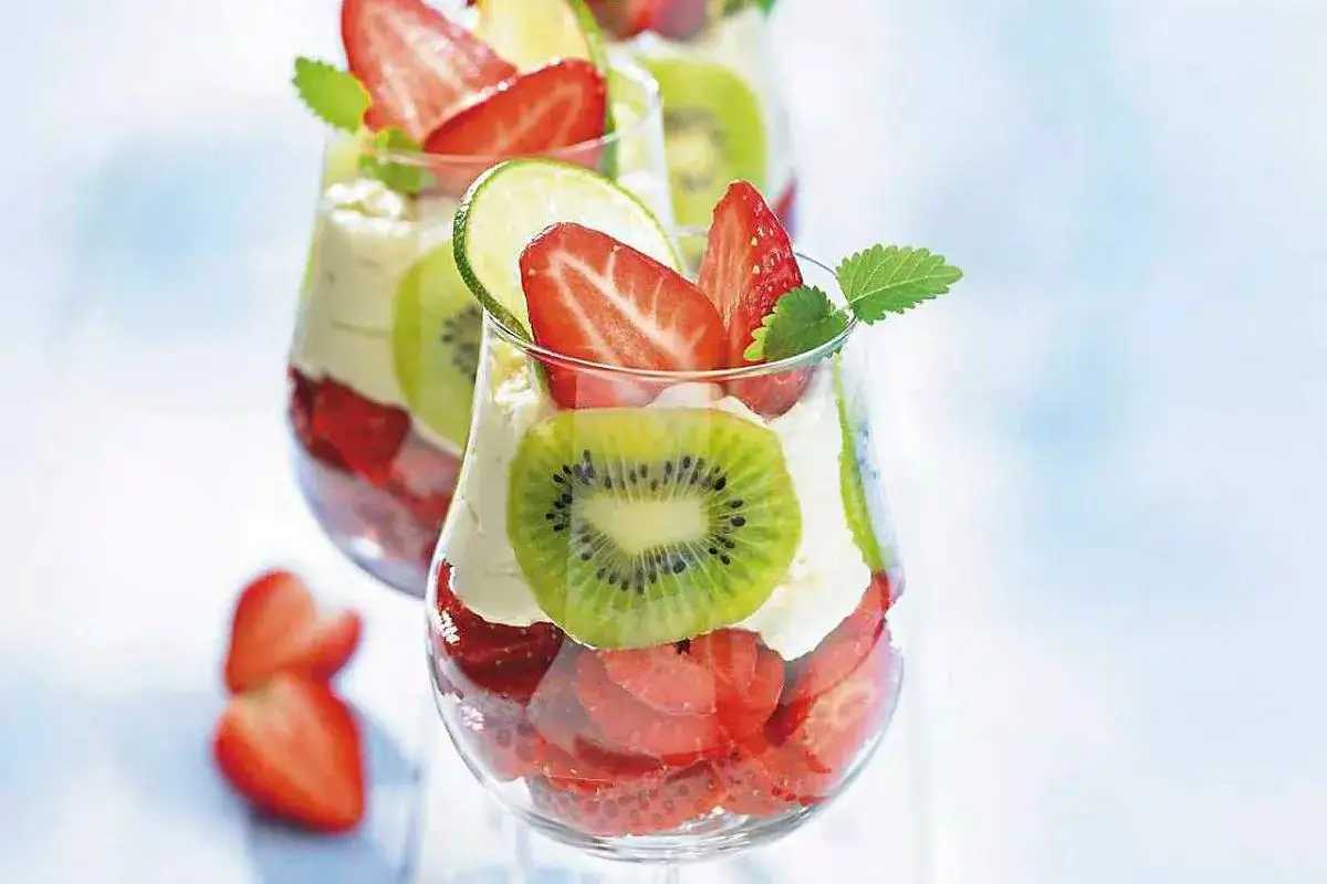Pyszny deser parfait z warstwami truskawek, kiwi i kremu, ozdobiony plasterkiem limonki i listkiem mięty.