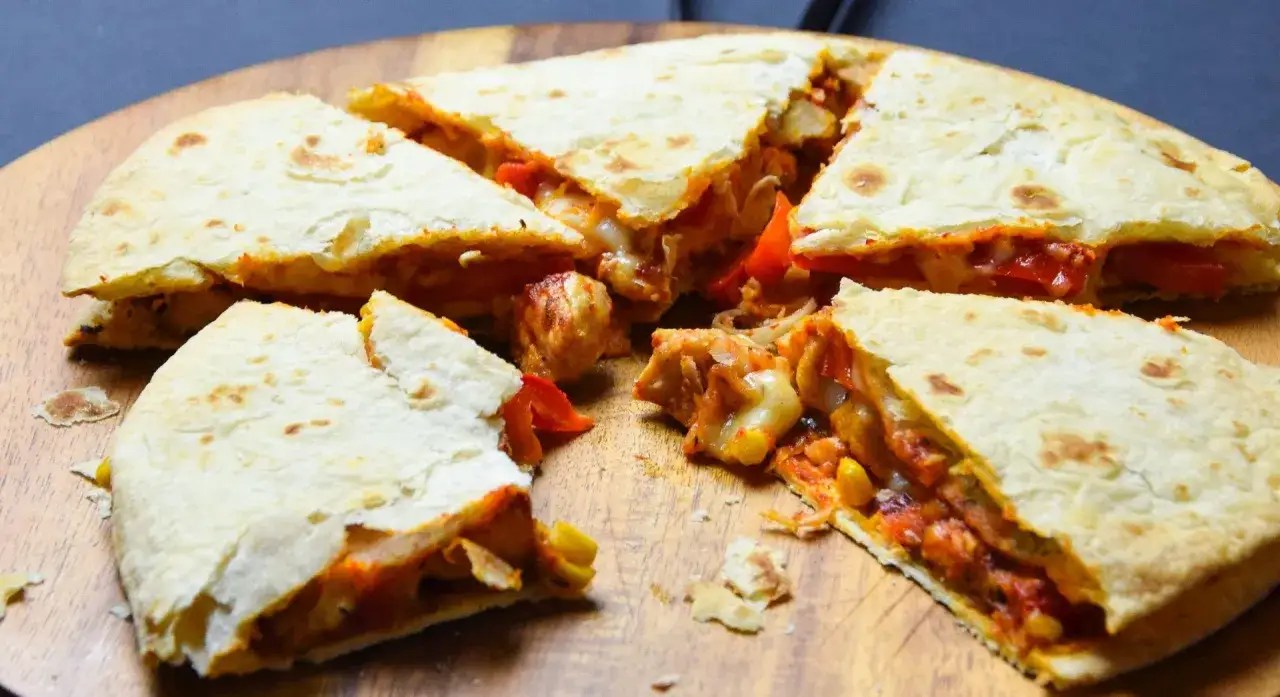 Pyszna quesadilla przepis z kurczakiem, papryką i kukurydzą, pokrojona na kawałki, prezentowana na drewnianej desce.