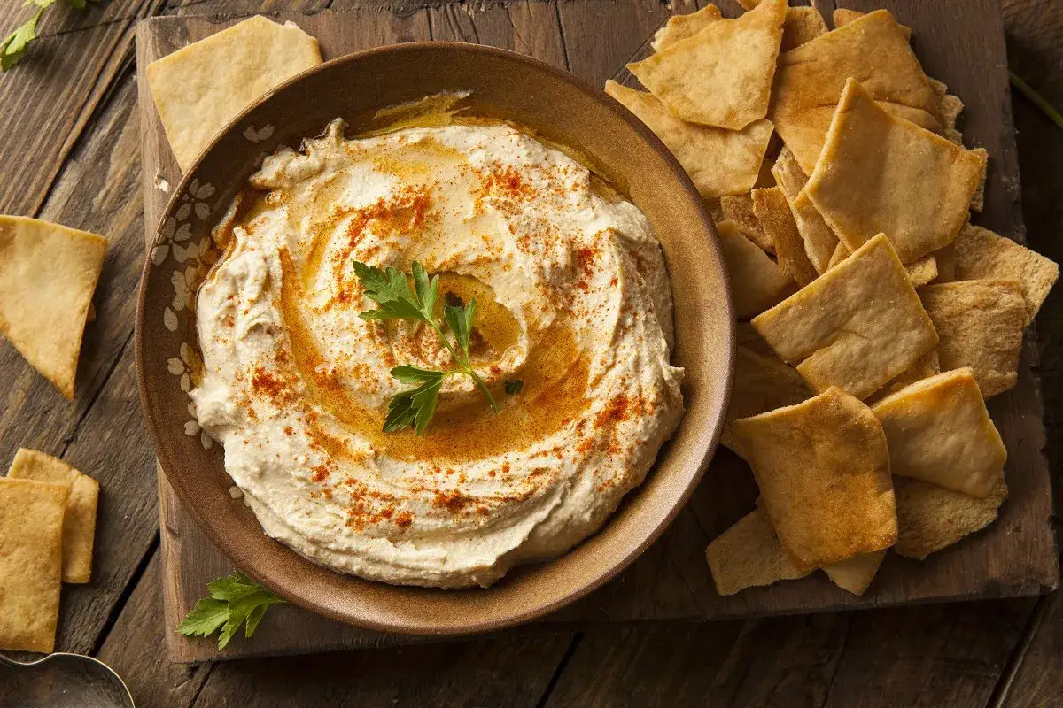 Kremowy hummus z papryką i natką pietruszki, podany z chrupiącymi kawałkami pity. Idealny na przekąskę, świetny przepis na hummus!