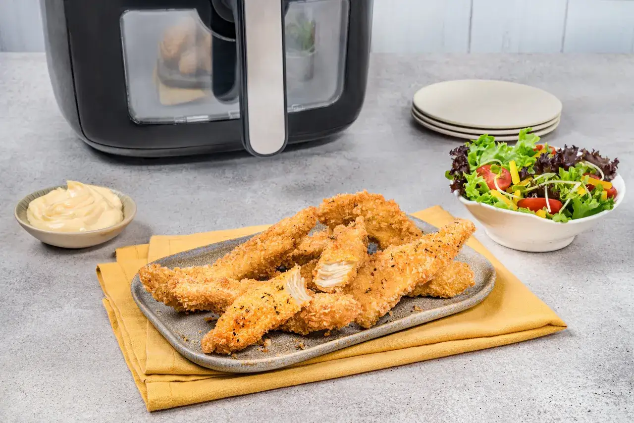 Chrupiący kurczak z airfryer na talerzu, obok sałatka i sos. Idealny obiad gotowy w kilka minut!