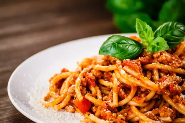 Talerz spaghetti bolognese z bazylią i parmezanem na drewnianym tle.