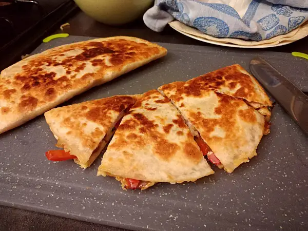 Złocista quesadilla, pokrojona na trójkąty, z widocznym nadzieniem z papryki. Idealny przepis na szybki posiłek.